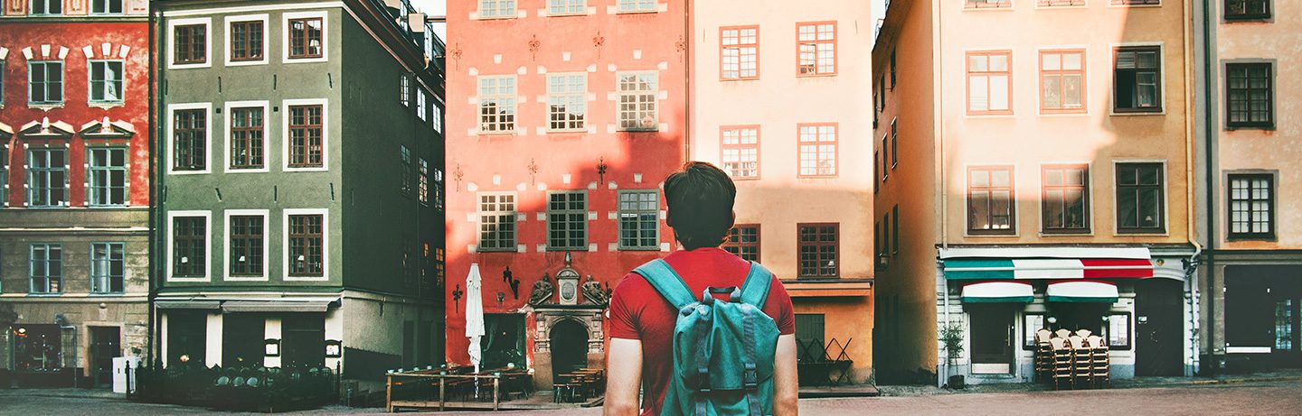 Ein Mann mit Rucksack steht vor bunten historischen Gebäuden auf dem Stortorget, einem Platz in Stockholm