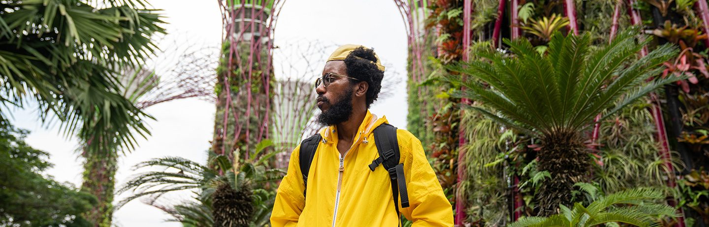 Man in a yellow jacket stands among tropical plants in the Gardens by the Bay CR: Stocksy
