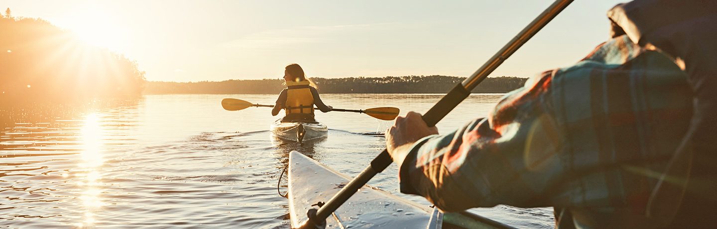 Two people paddling kayaks across a calm lake at sunset