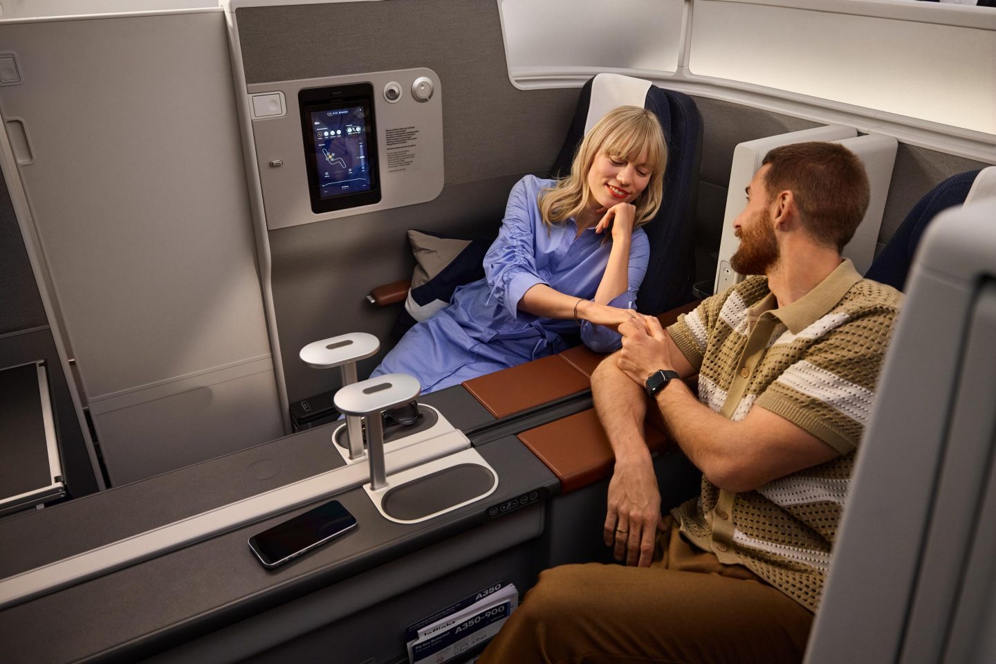 A smiling couple holding hands in a spacious premium airline cabin.