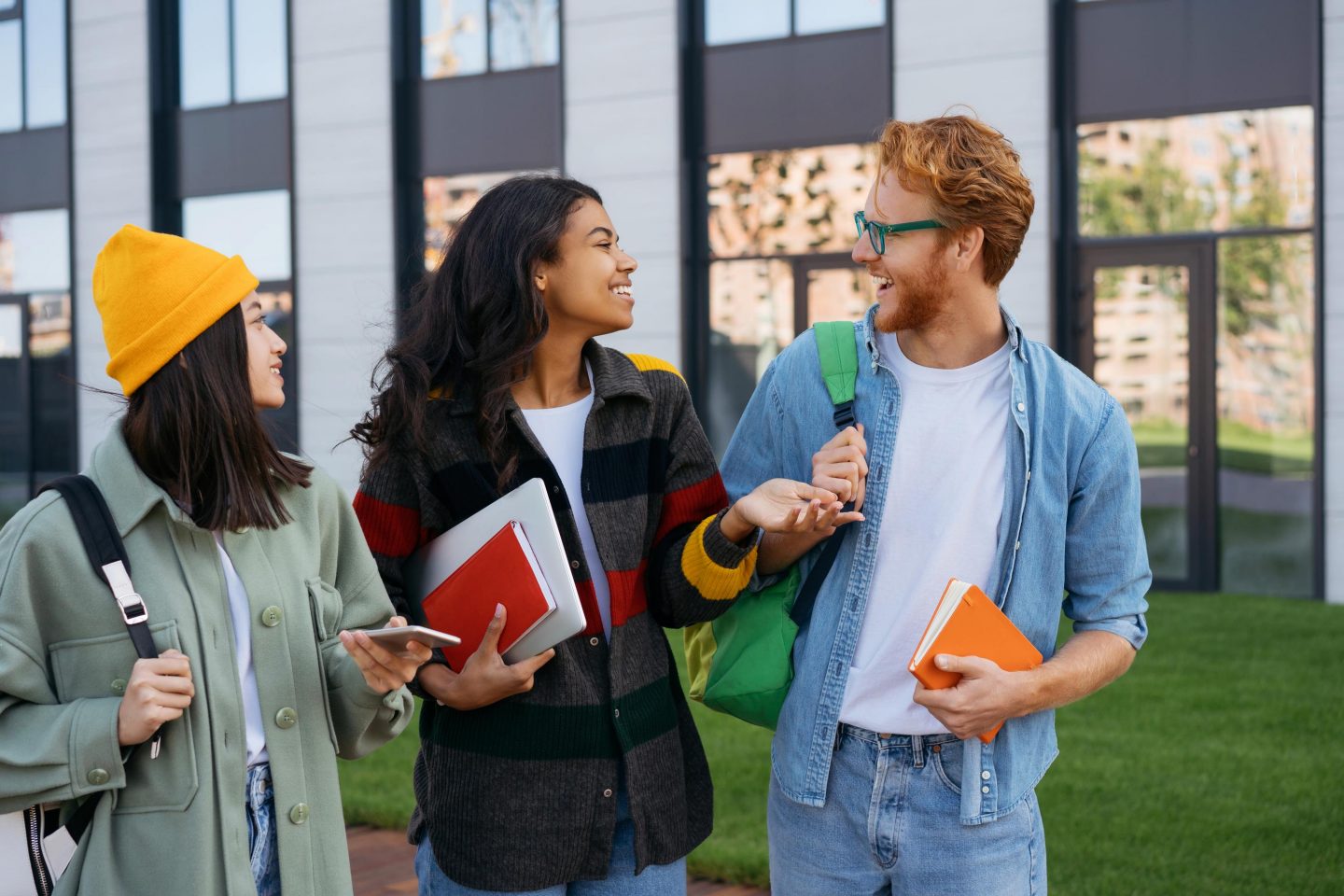 Eine Gruppe l&radic;&sect;chelnder Studenten geht mit B&radic;&ordm;chern und Rucks&radic;&sect;cken auf dem Universit&radic;&sect;ts Campus spazieren und unterh&radic;&sect;lt sich. // Group of smiling students with books and backpacks walking on university campus, talking.