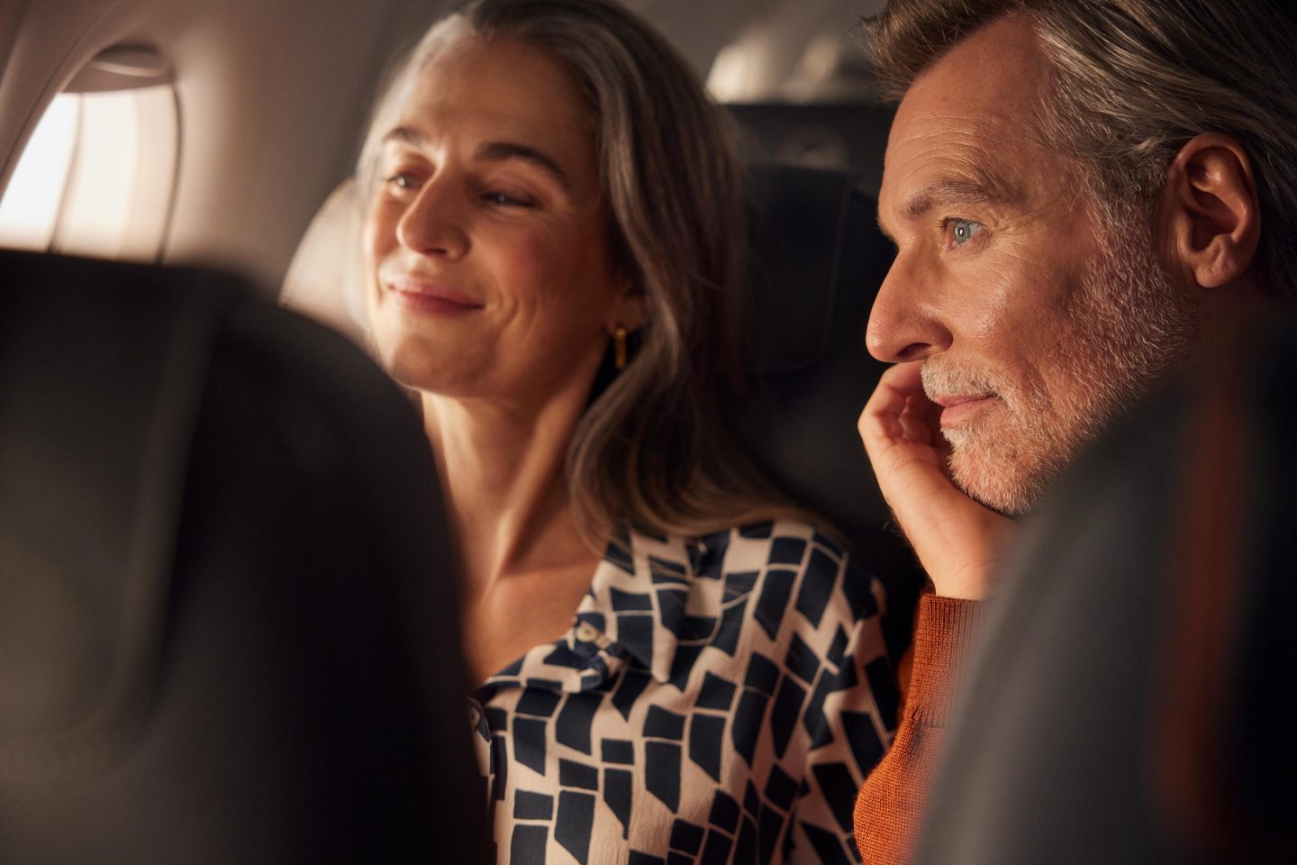 Endlich geht die Reise los, zwei ältere Reisende blicken erwartungsvoll aus dem Flugzeugfenster.