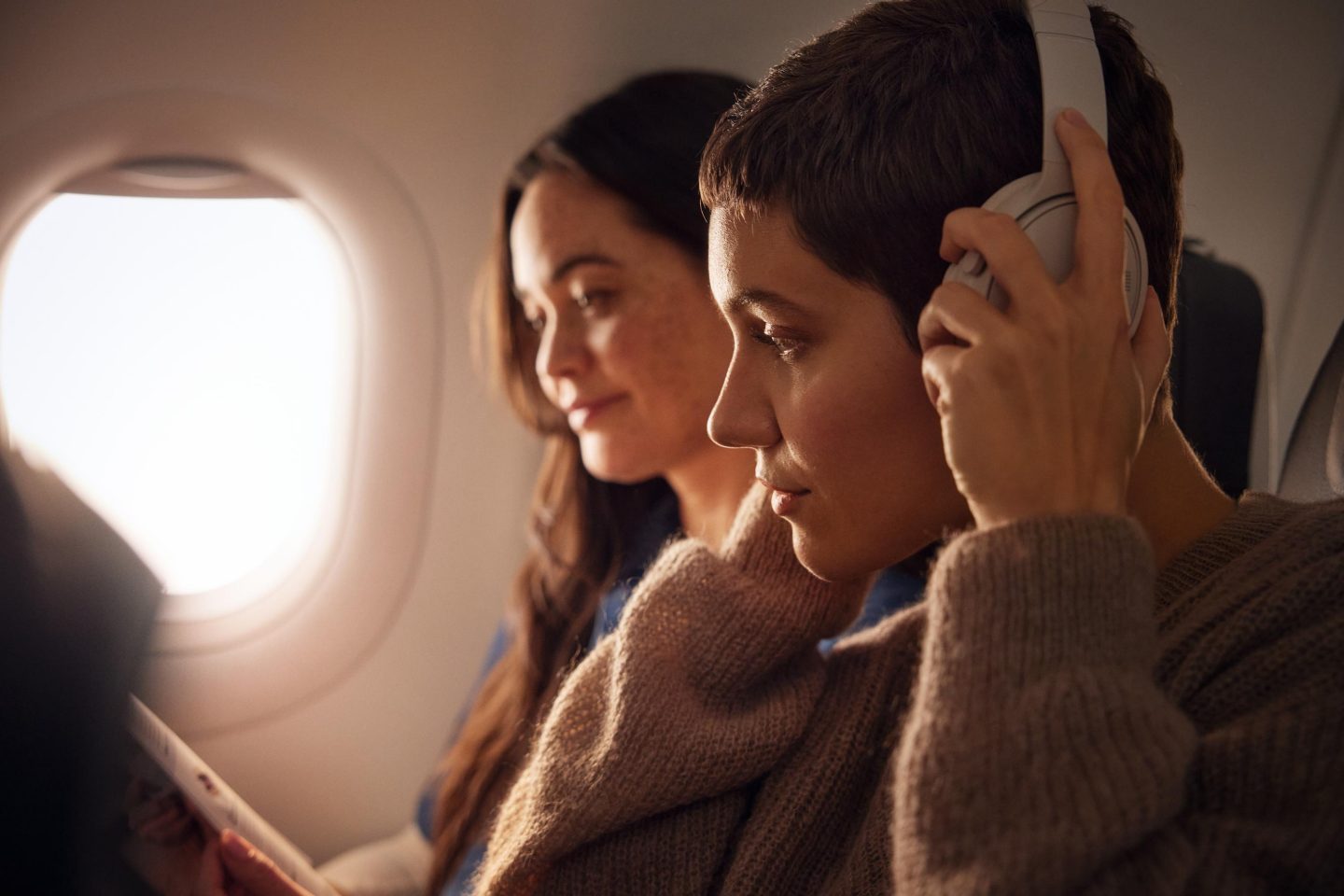 Zwei Frauen entspannen sich mit Kopfhörern und einem Buch im Flugzeug.