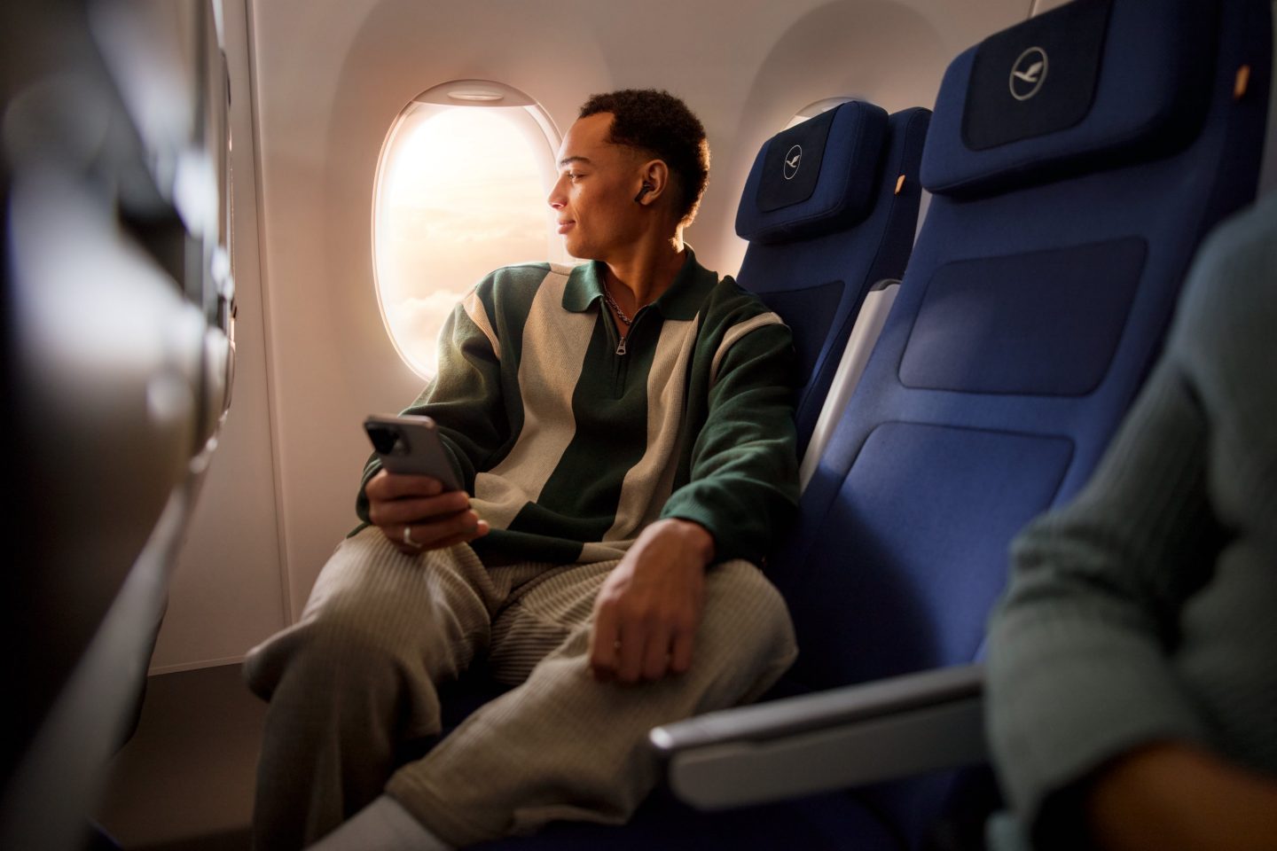 Ein Mann sitzt entspannt in der Economy Class und h&auml;lt sein Handy in der Hand // A man is sitting relaxed in economy class, holding his cell phone