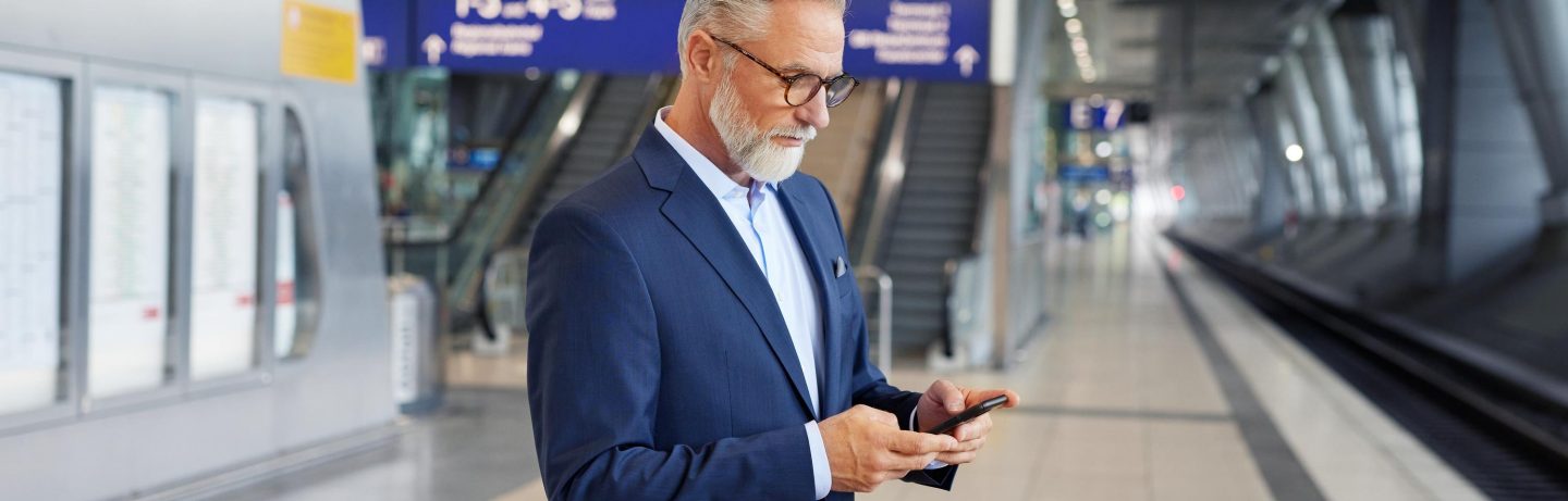 Businessman with a smartphone standing at a train station