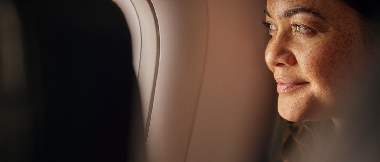 A woman looks thoughtfully out of an aeroplane window.