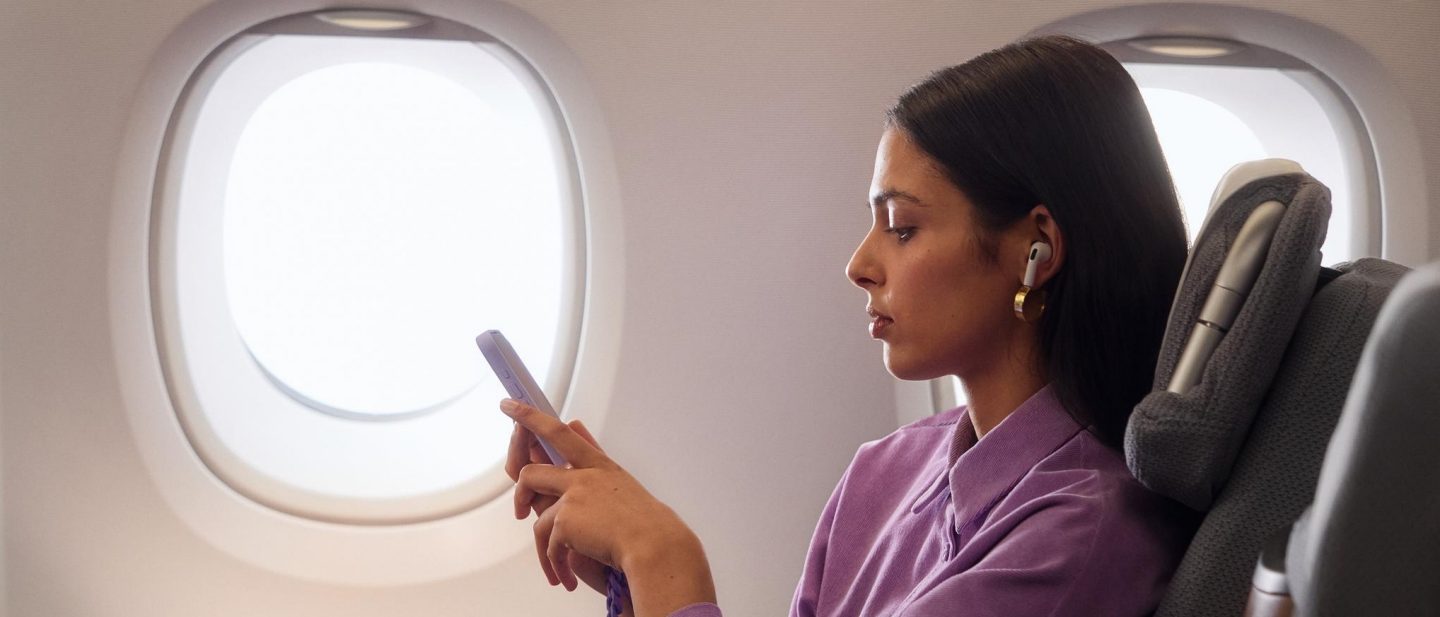 Eine junge Frau sitzt in der Business Class im A380 und schaut auf ihr Smartphone.