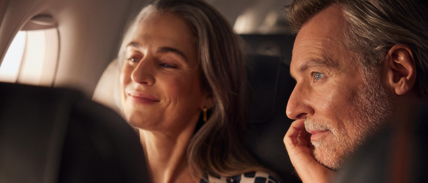 A couple sit together in a plane looking happy and relaxed.