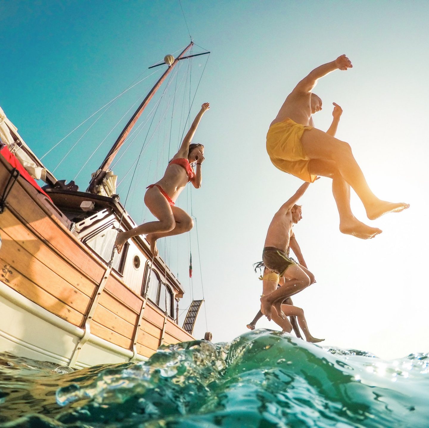 Happy friends jumping from a sailing boat into the sea.