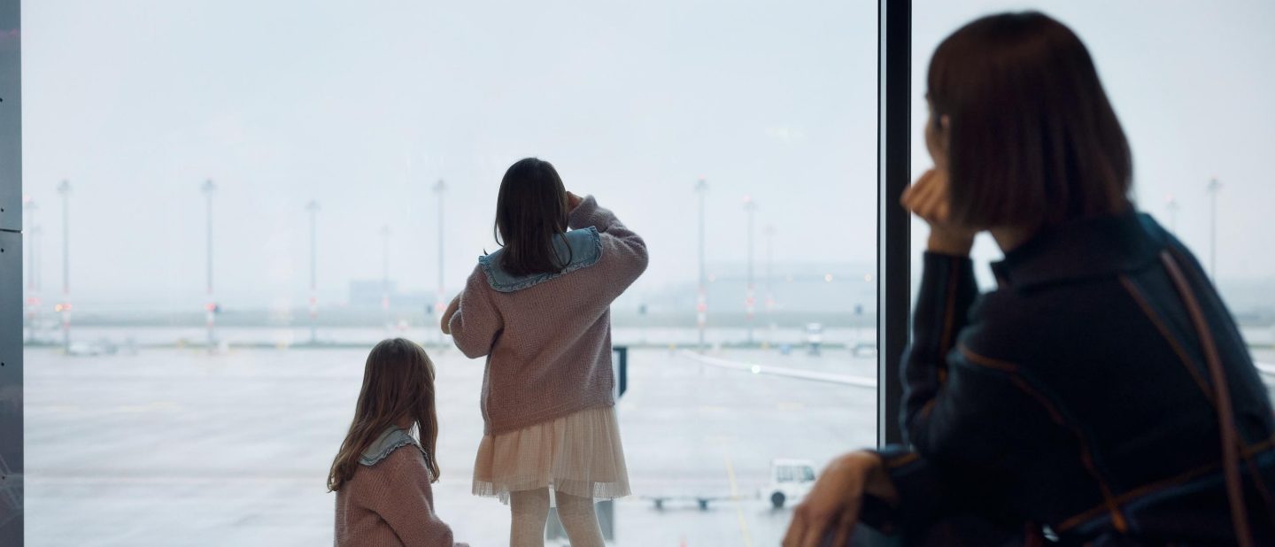 Eine Familie wartet am Gate und schaut raus auf das Flughafengel&auml;nde. // A family waits at the gate and looks out onto the airport grounds.