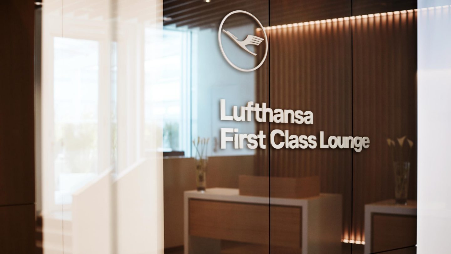 Entrance to the Lufthansa First Class Lounge featuring a glass facade, Lufthansa branding, warm wood paneling, and soft lighting that creates an elegant and exclusive atmosphere.