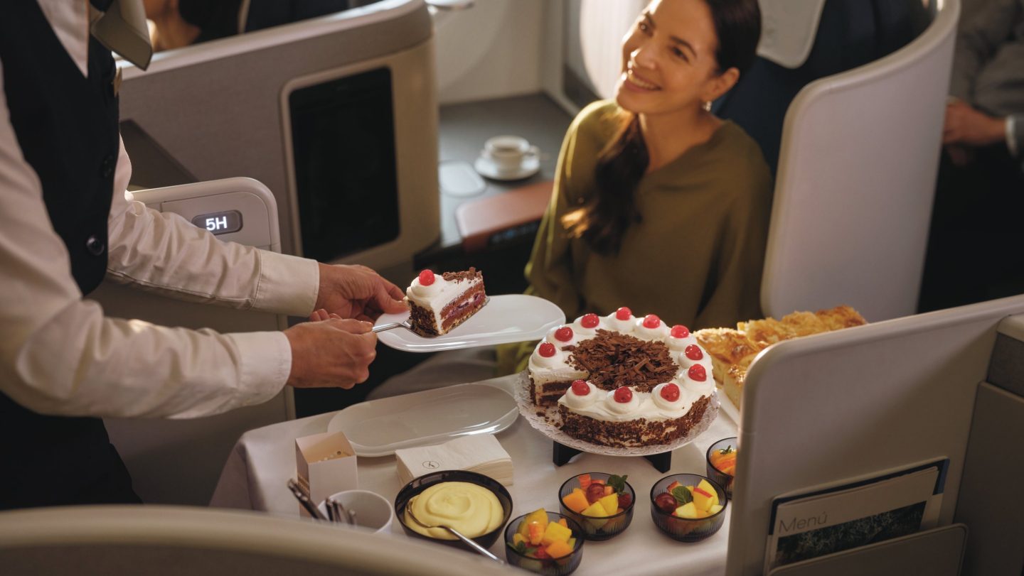 Smiling passenger enjoys delightful desserts and attentive service in our premium cabin.
