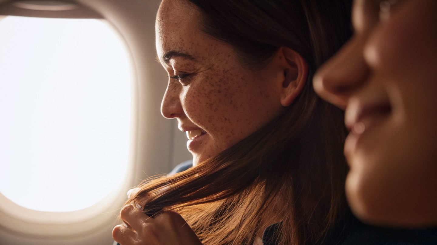 Primer plano de dos pasajeros sonrientes a bordo de un avión.