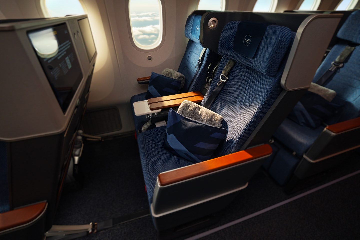Lufthansa premium economy cabin with blue seats, wooden armrests, and personal entertainment screens.