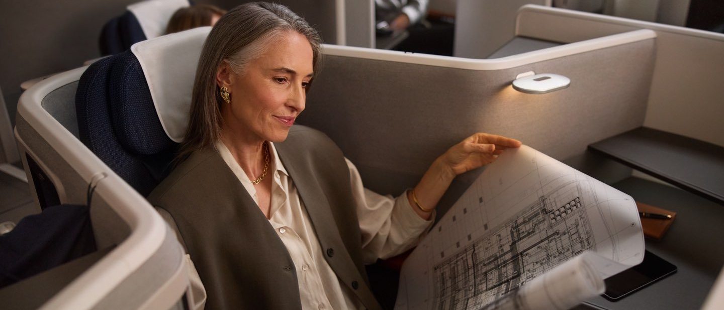 Woman reviewing architectural blueprints while sitting in a spacious, private airplane cabin seat.