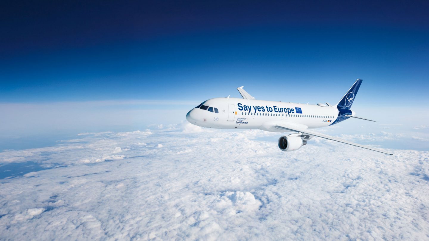 Aircraft 'Say yes to Europe' flying above clouds under a blue sky.