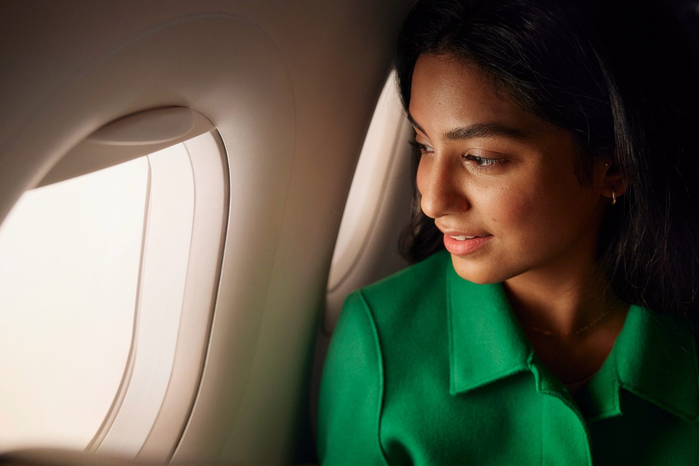 Une femme habillée en vert regarde par le hublot d’un avion et profite de la vue.