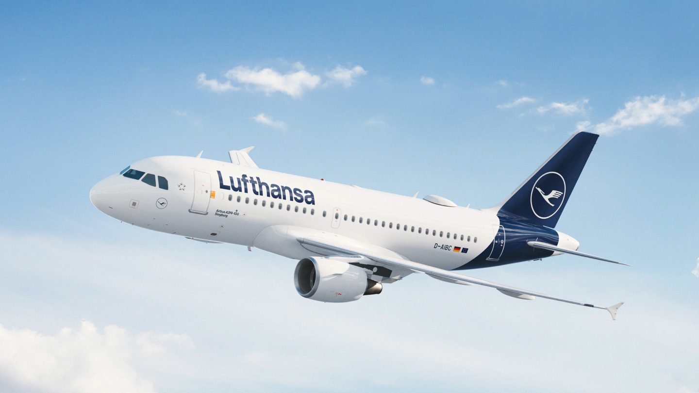 Un Airbus A319-100 de Lufthansa vole dans un ciel bleu parsemé de nuages blancs.