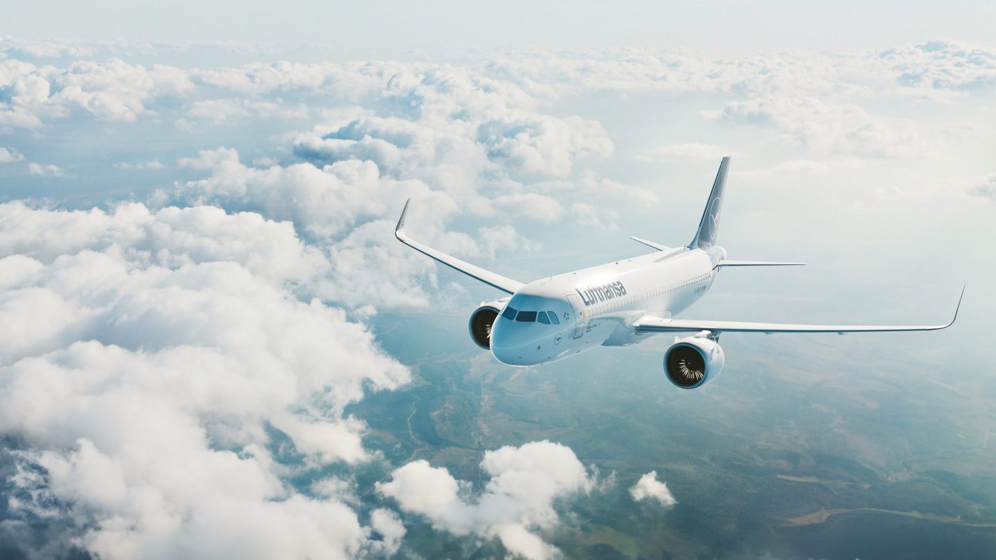 Lufthansa airplane flying above white clouds, land visible below.