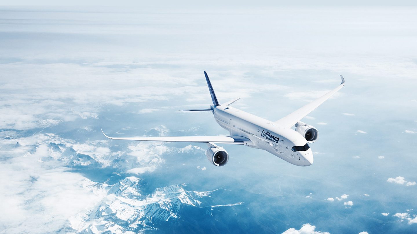 Lufthansa aircraft flying over snow-capped mountains and clouds.