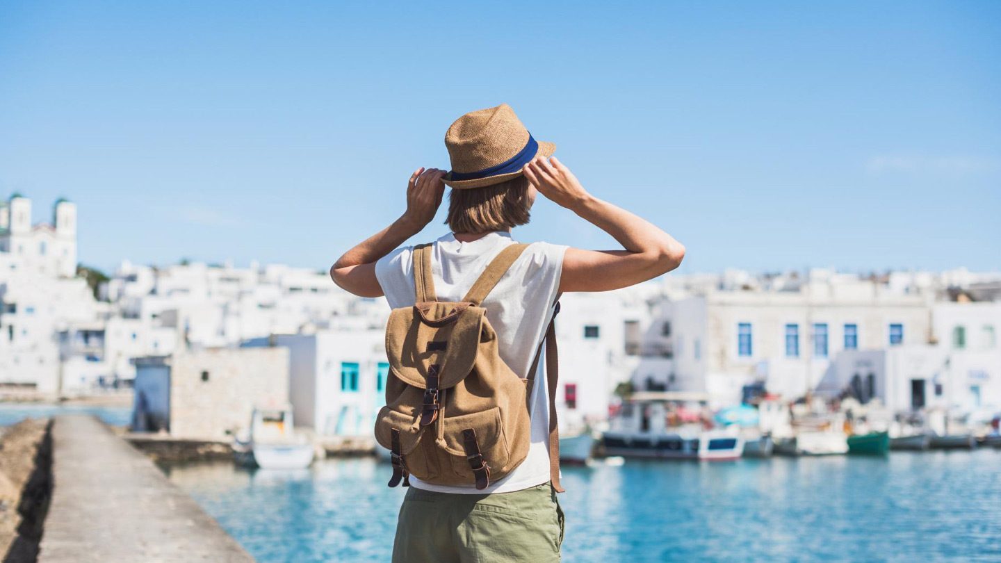 Backpacker with hat admiring a beautiful Greek island village by the sea.