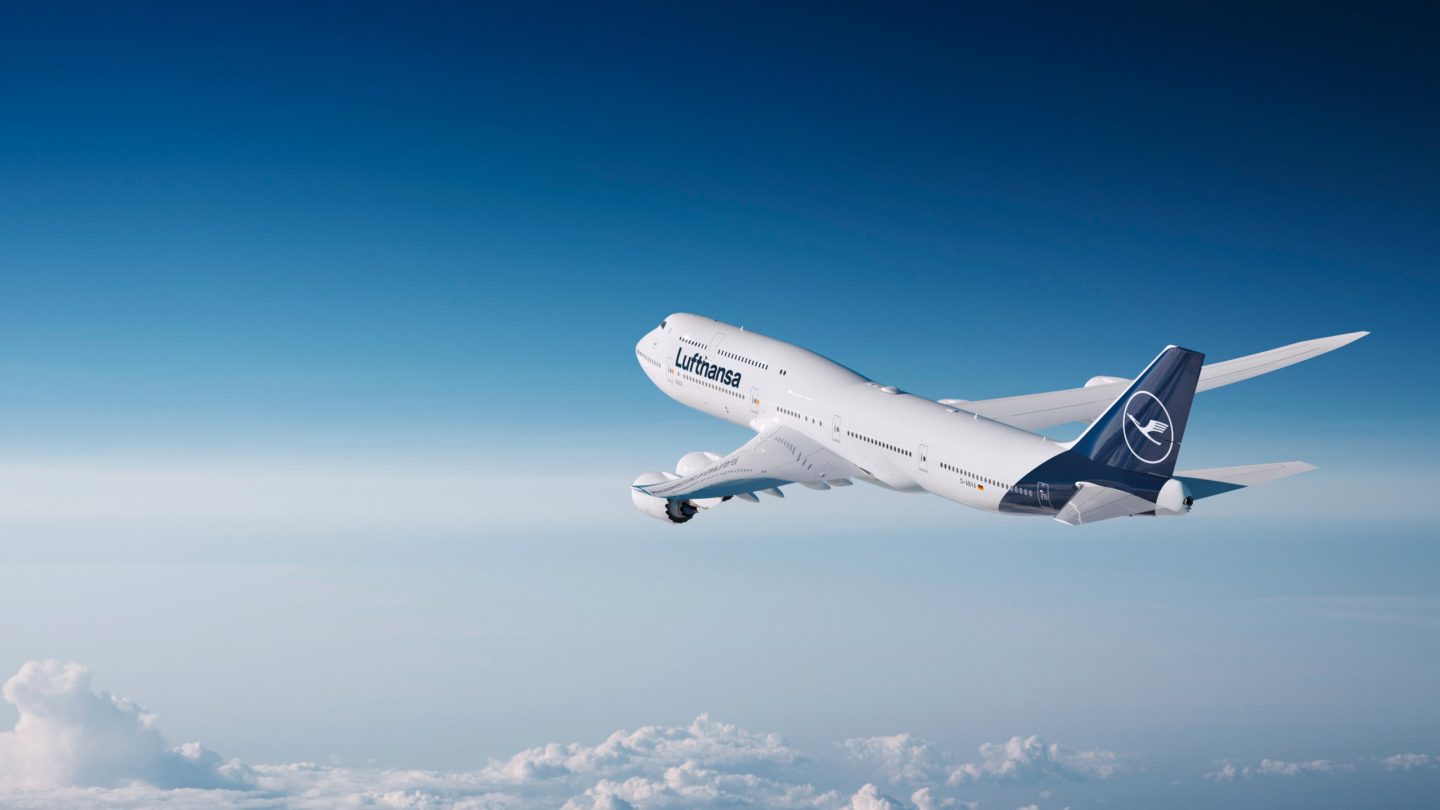 Lufthansa jet cruising above a sea of clouds under a vast blue sky.