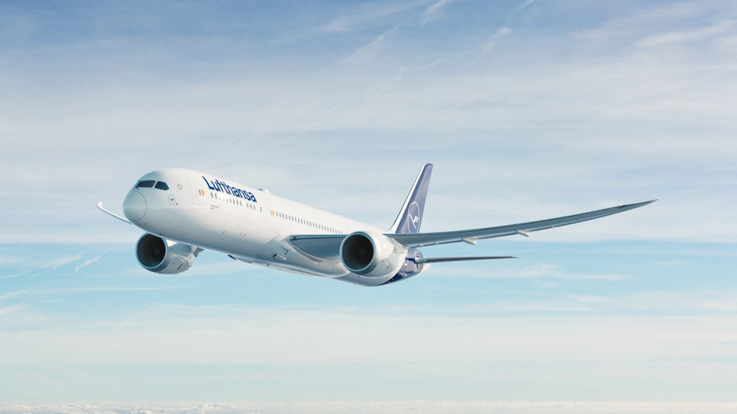 Boeing 787-9 Dreamliner flying through blue sky with light clouds.