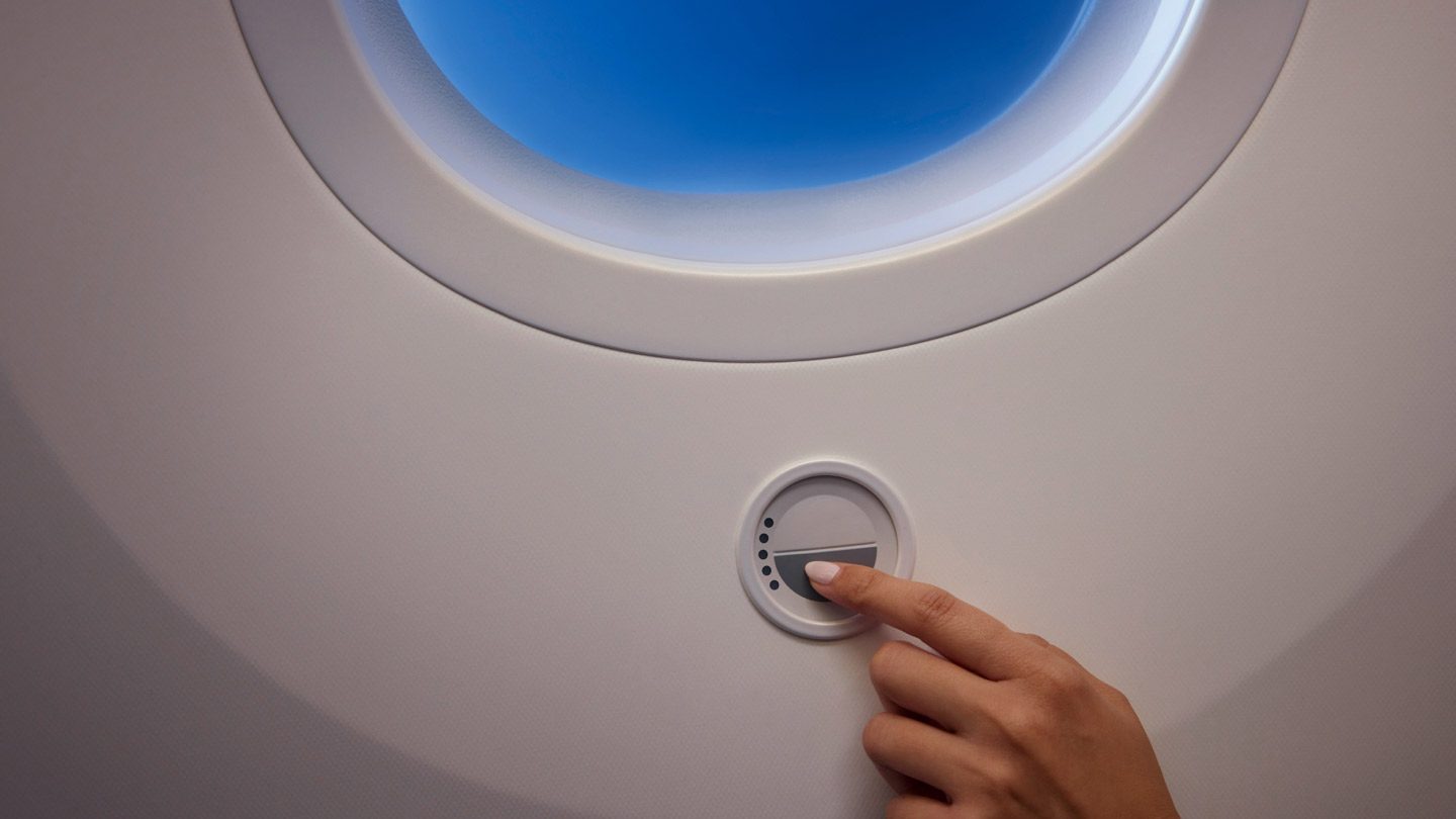 Hand adjusting the electronic dimmer control below a round airplane window.