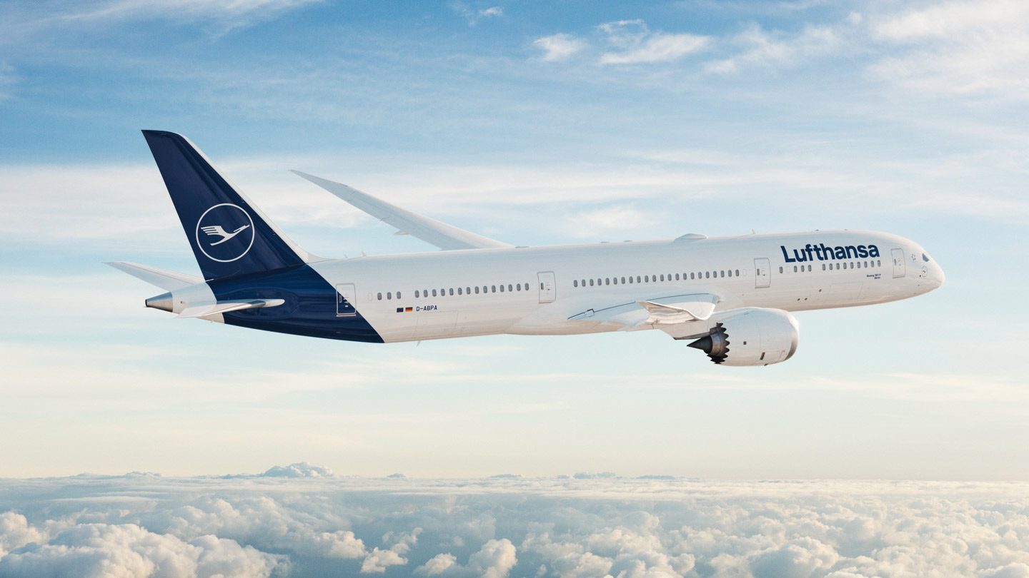 Side profile of a Lufthansa Boeing 787-9 flying over mountains.