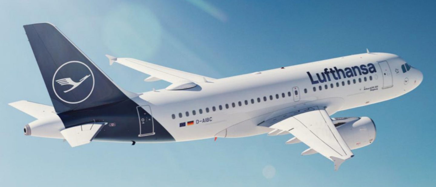 Lufthansa airplane with crane logo flying against a clear blue sky.