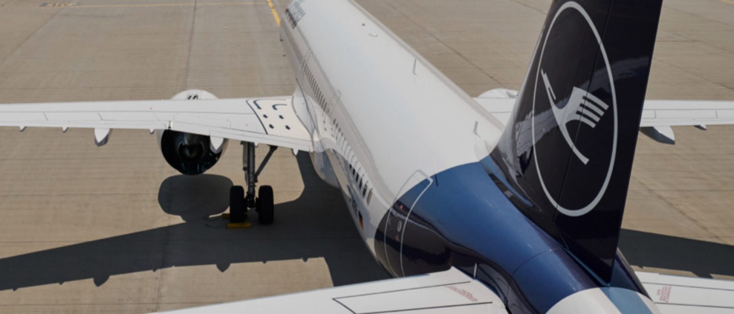 Lufthansa plane on tarmac with blue tail and crane logo.
