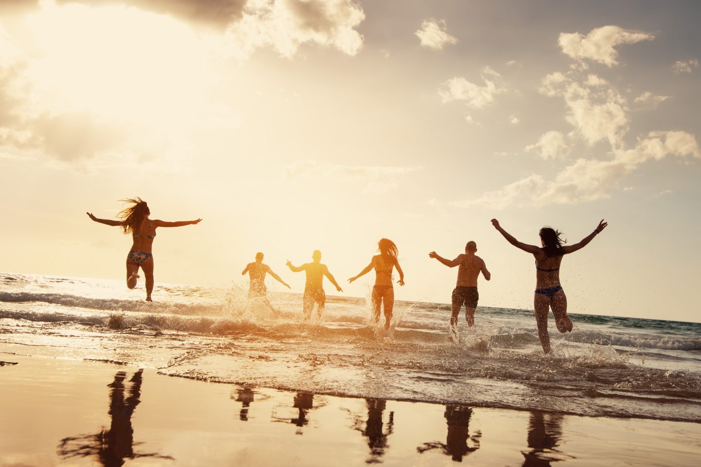 Silhouettes of happy friends runs at sunset sea beach. Beach vacations concept