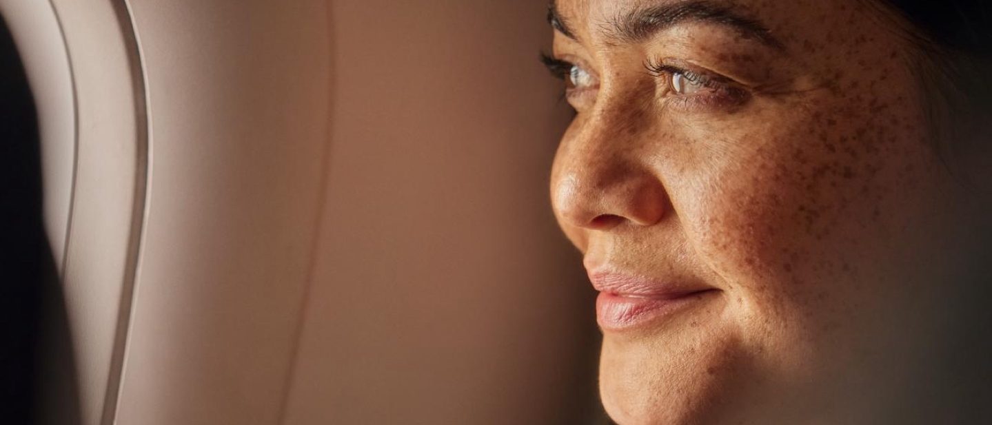 Eine Frau blickt nachdenklich aus dem Flugzeugfenster.