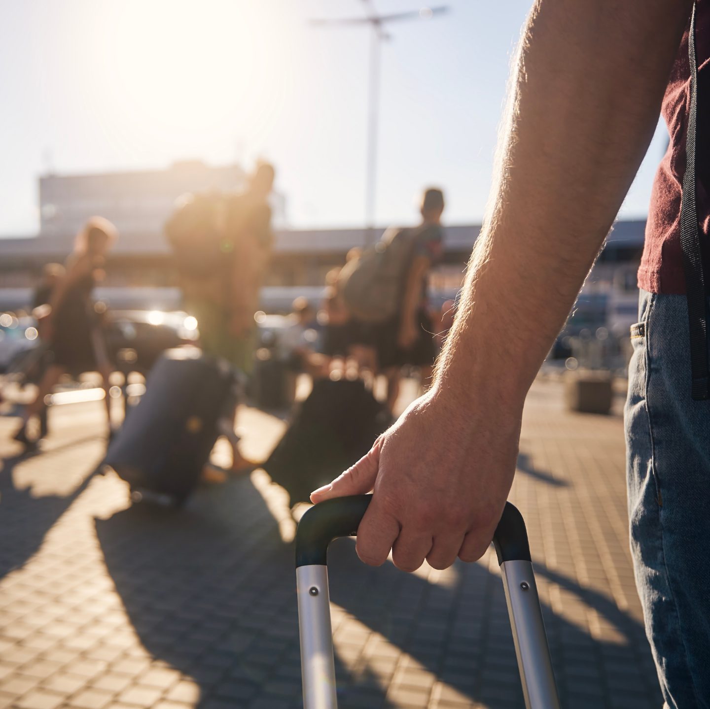 Hand holding a suitcase at a sunny airport.