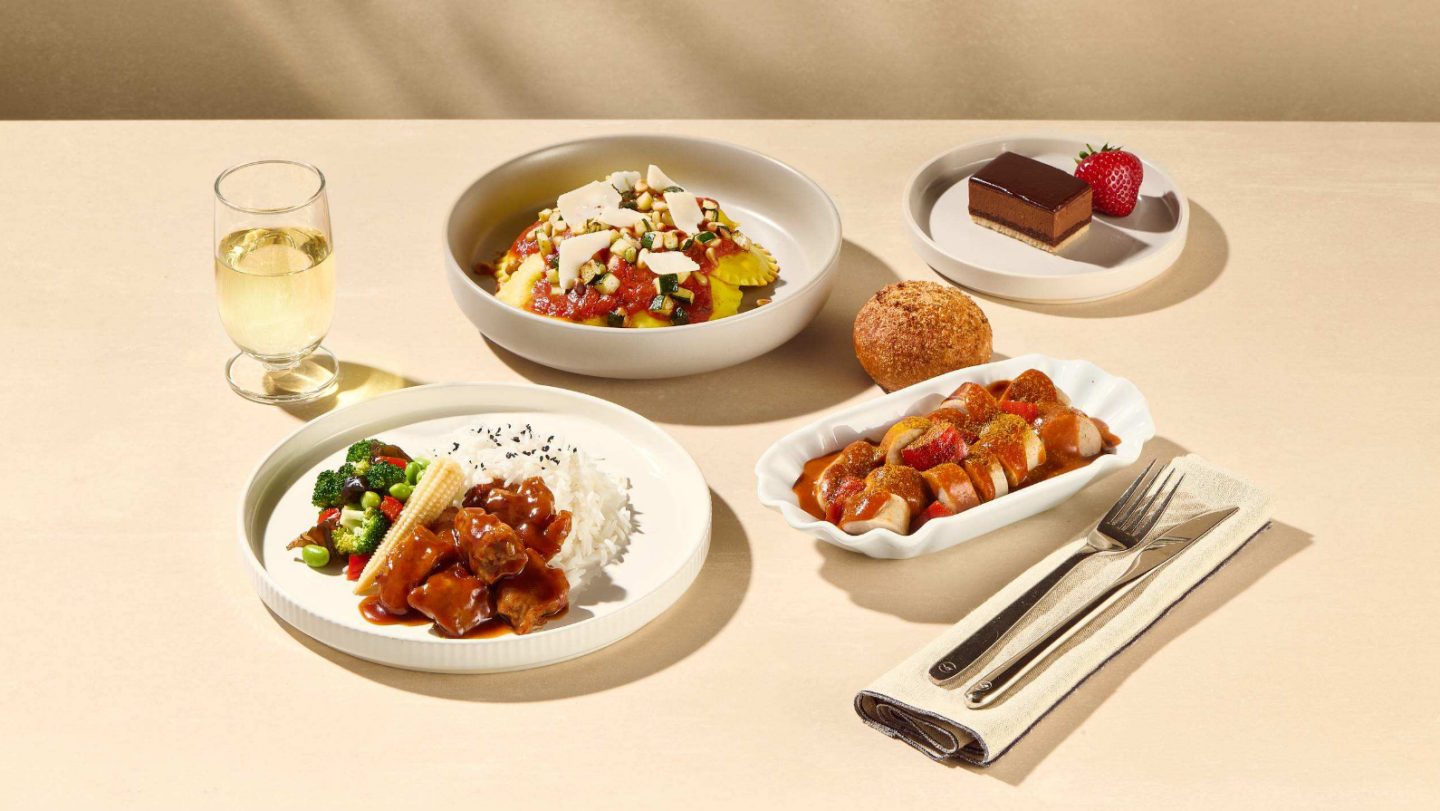 Assorted meal dishes including ravioli with tomato sauce, rice with vegetables and meat, sliced sausage with sauce, a bread roll, chocolate dessert with a strawberry, and a glass of white wine.