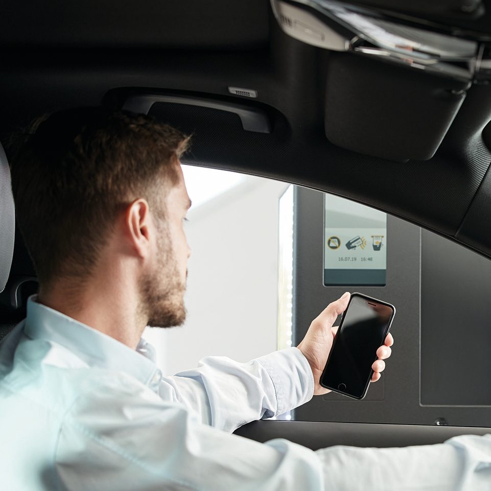 A man in a car scanning his smartphone at a parking terminal.