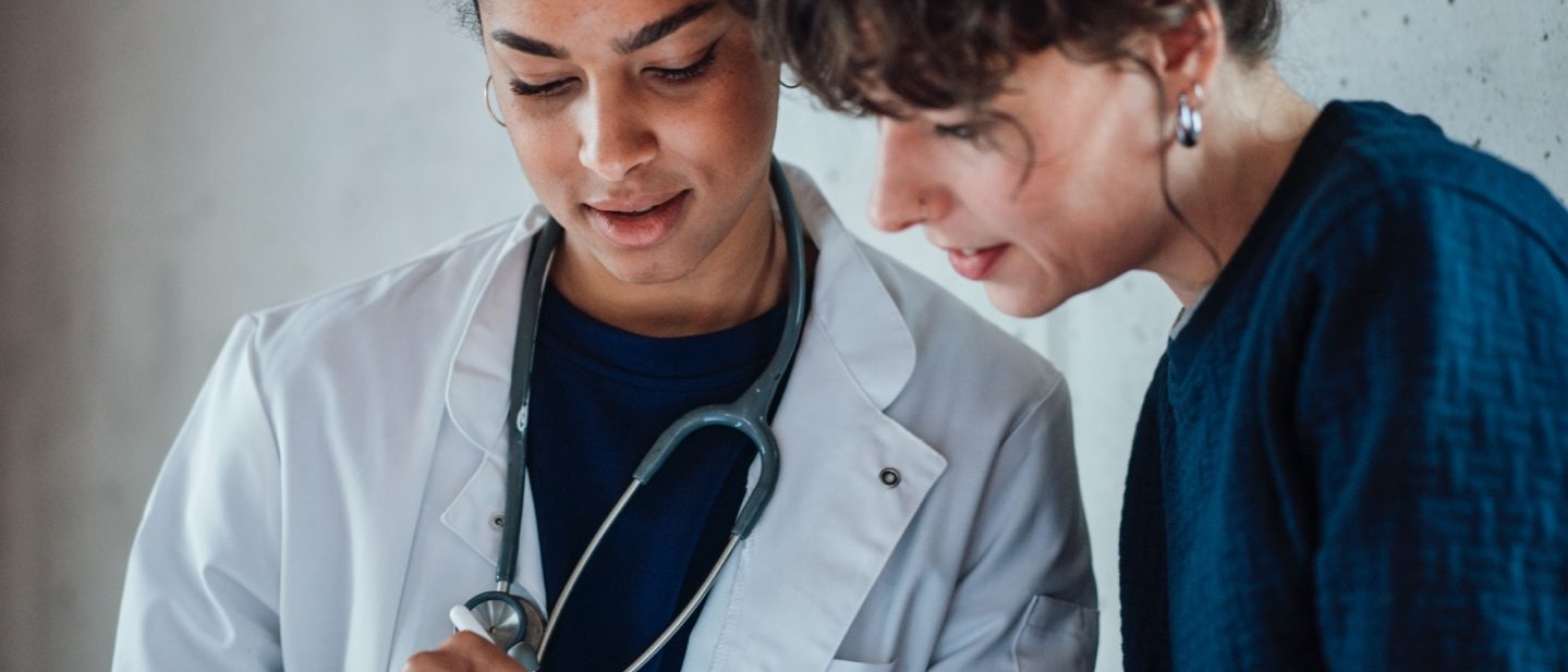 Eine Ärztin mit Stethoskop und eine Patientin schauen gemeinsam auf ein Tablet.