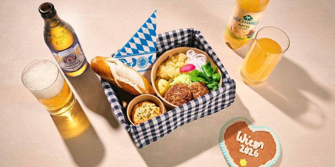 Ein karierter Korb mit Onboard Delights Menüs, umgeben von Getränken und einem Wiesn-Lebkuchenherz