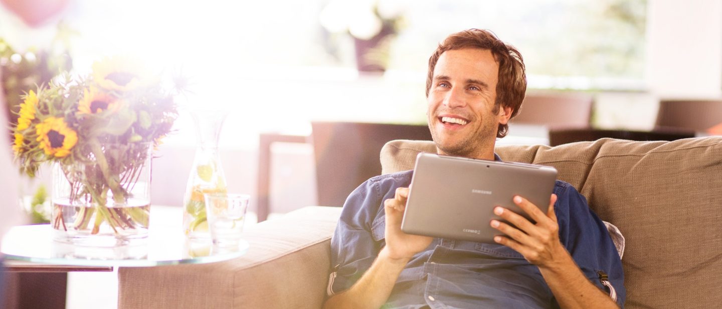 Mann sitzt auf der Couch und hat ein Tablet in der Hand __ Man is sitting on the couch and has a tablet in his hand