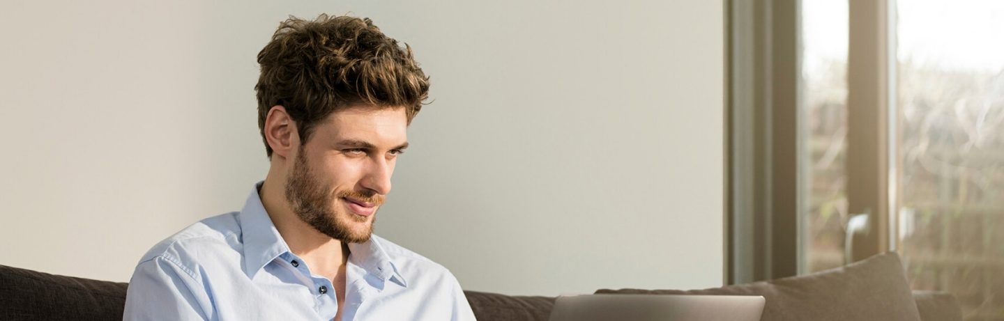 Germany, handsome man sitting on couch in modern design living room working on laptop in front of large garden window (Germany, handsome man sitting on couch in modern design living room working on laptop in front of large garden window, ASCII, 118 co