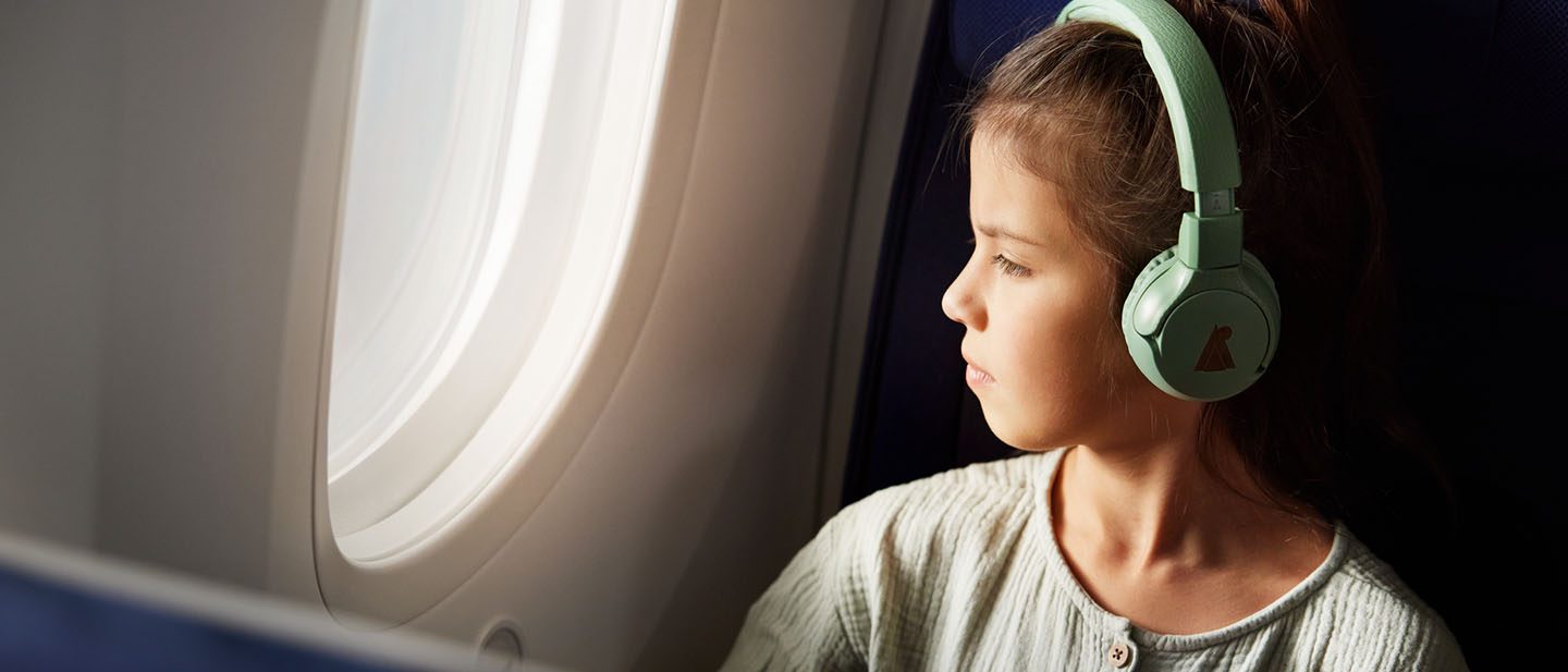 Girl with headphones sits on the plane and looks out of the window.