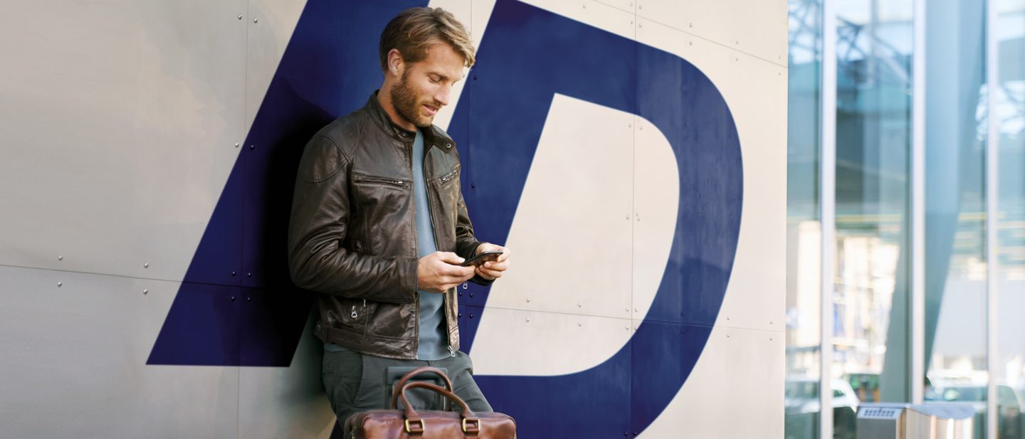 Junger Mann mit Smartphone in der Hand. Er meldet sich mit seiner Travel ID/E-Mail Adresse in seinem Konto an.