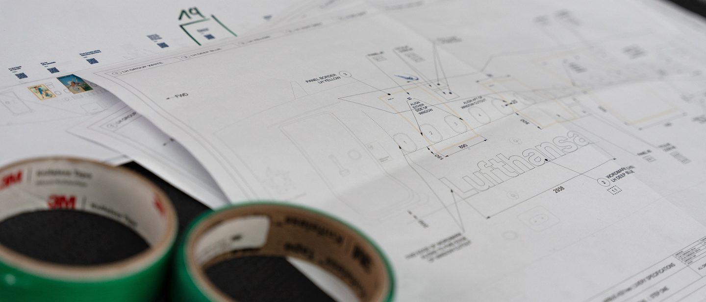 Technical drawings for aircraft livery beside rolls of tape on a table.
