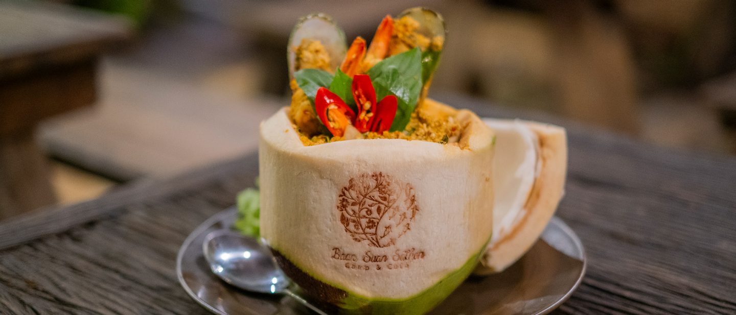 Exotic seafood dish served in a coconut with shrimp, spices, and a decorative red chili.