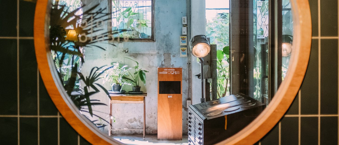 Vintage-style cafe interior with ornamental plants, rustic decor, and a reflective circular mirror.