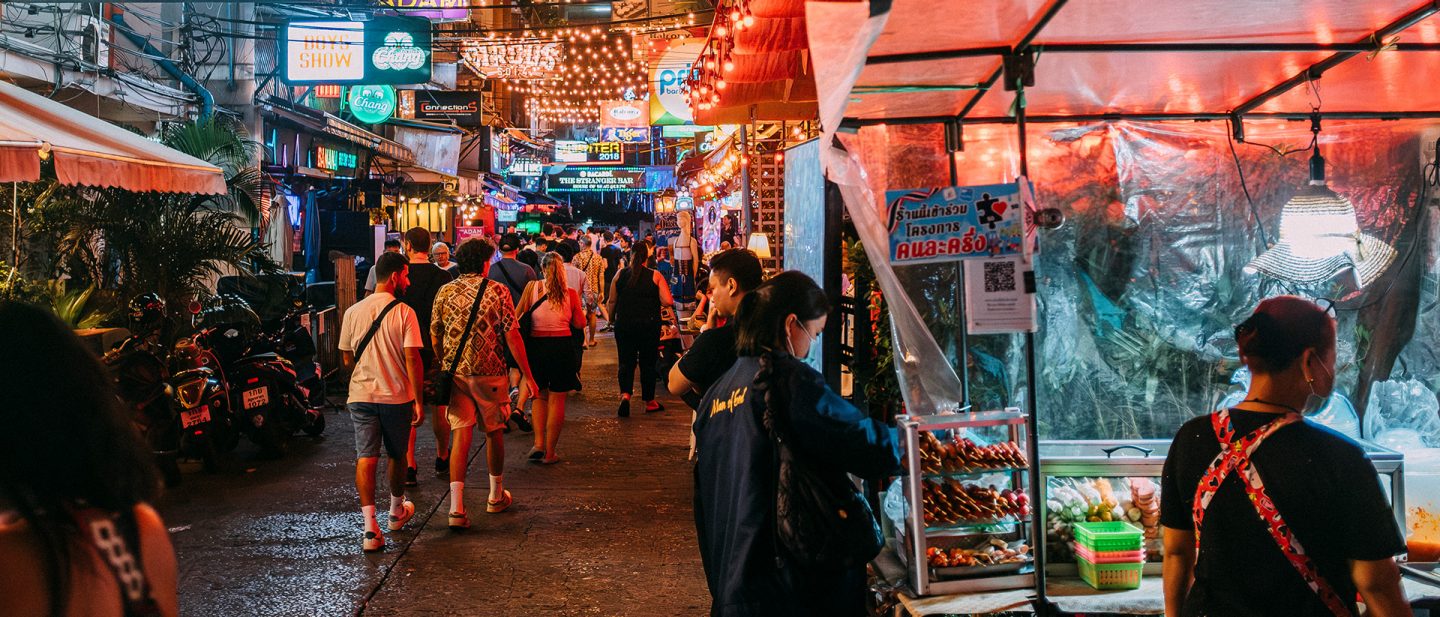 Vibrant street scene at night in an Asian market with crowds, neon signs, and street food stalls.