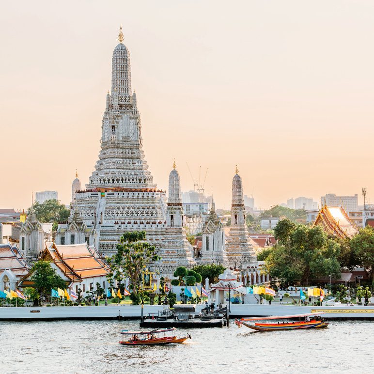 Wat Arun temple at sunset with boats on the Chao Phraya River in Bangkok, Thailand.