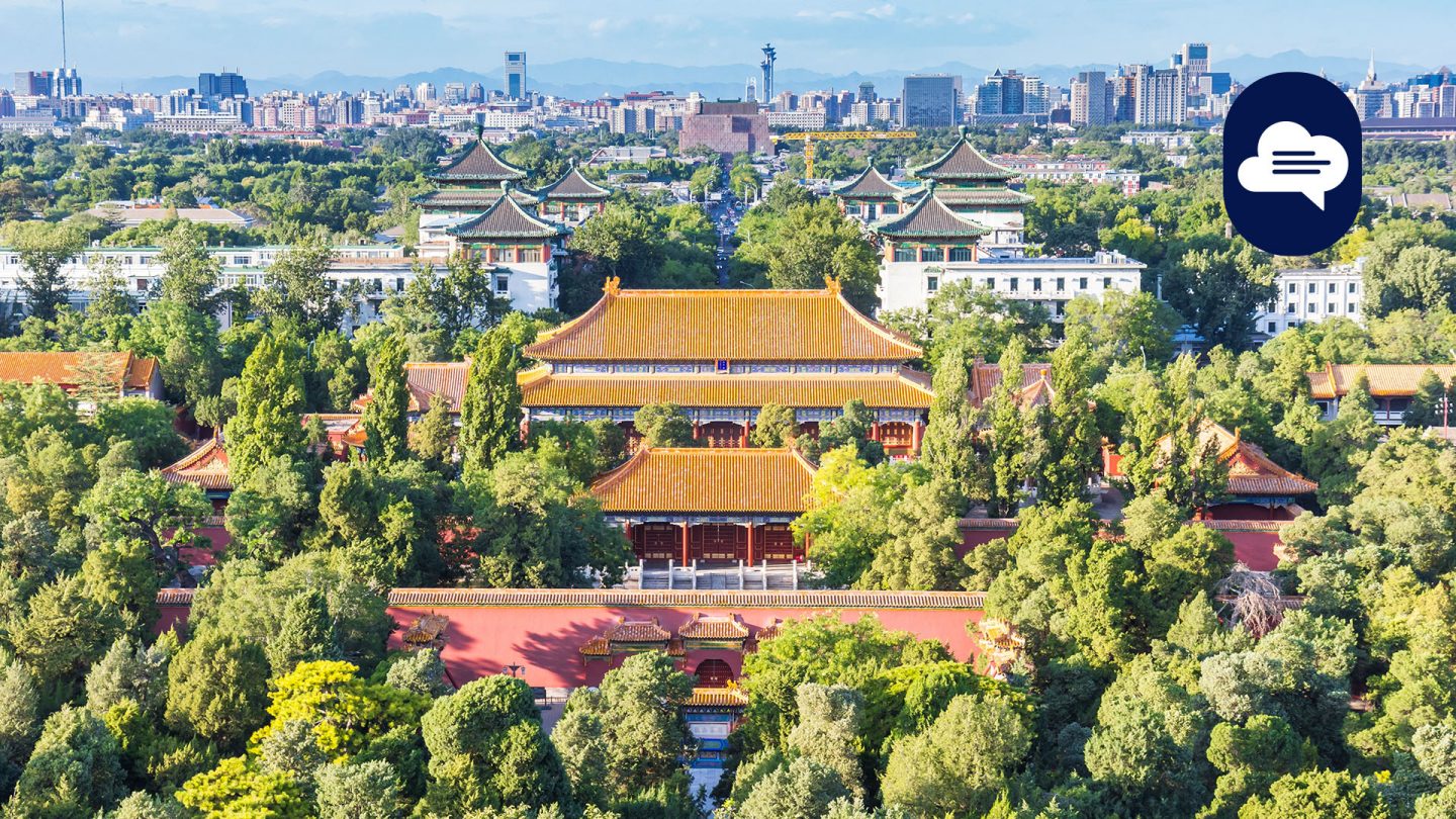 Aerial view of a traditional temple complex with orange roofs, surrounded by dense greenery and a modern skyline in the background.