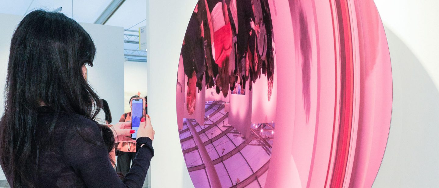 Woman photographing a large reflective pink art installation in a gallery in Seoul