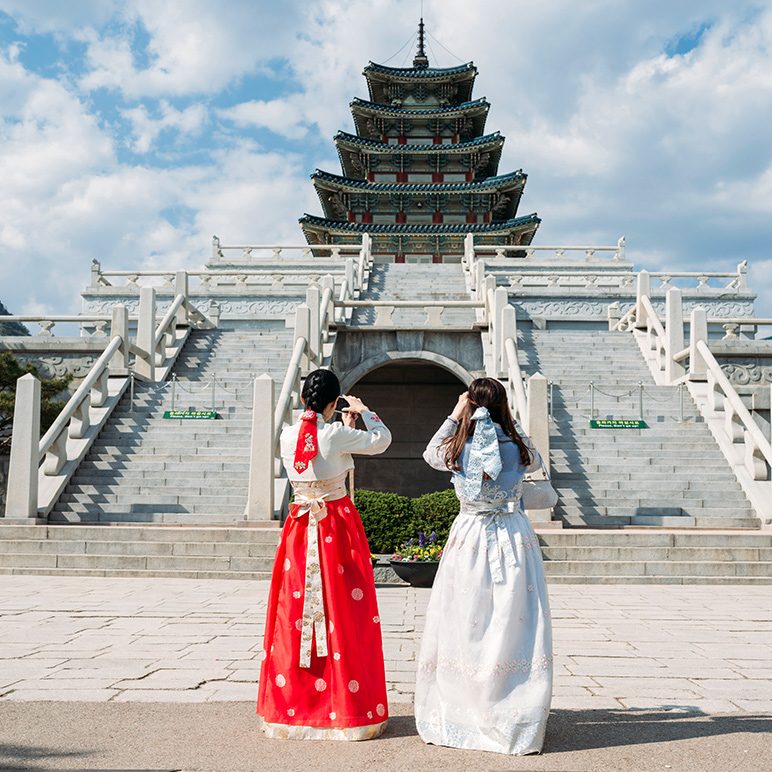 Two women in traditional Korean hanboks taking photos at a historic pagoda in Seoul